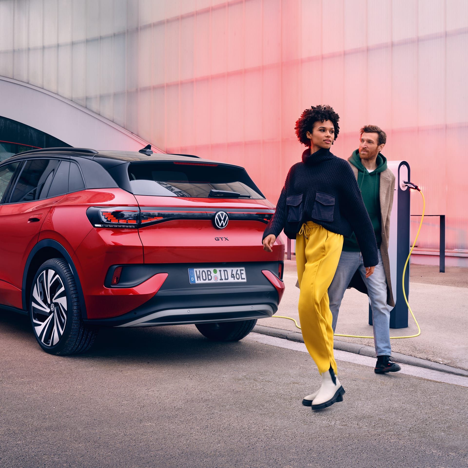 Pogled od zadaj na rdeči VW ID.4 GTX, pred katerim dve osebi prečkata ulico