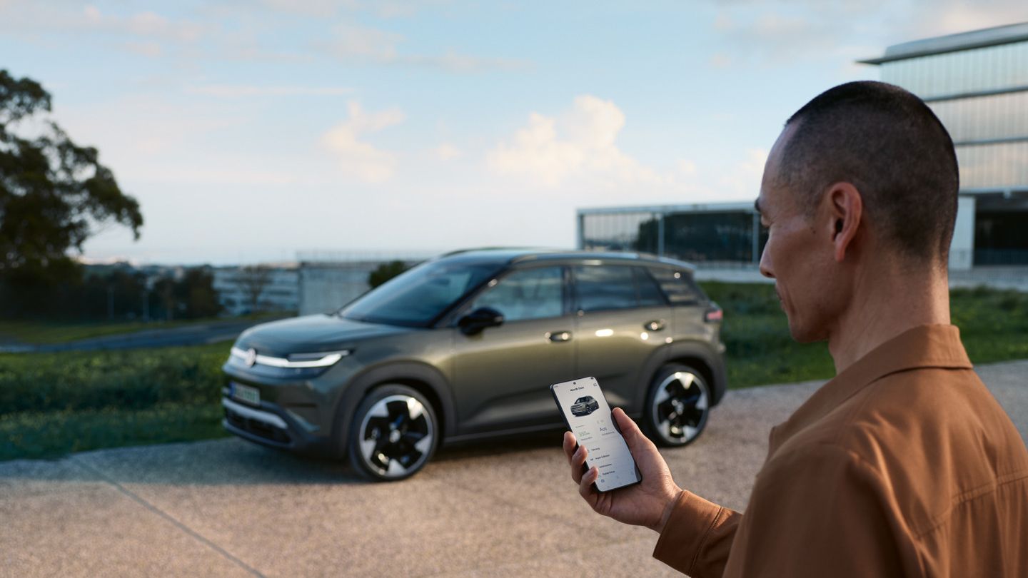 Ein grüner VW ID.Cross parkt an einem Wohnhaus, daneben steht ein Mann und schaut auf sein Smartphone.