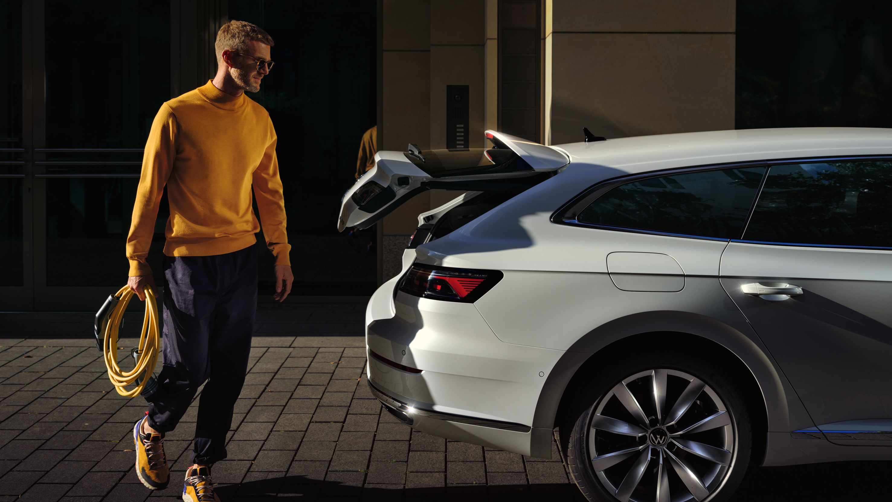 Moški s polnilnim kablom v roki zraven Arteona Shooting Brake