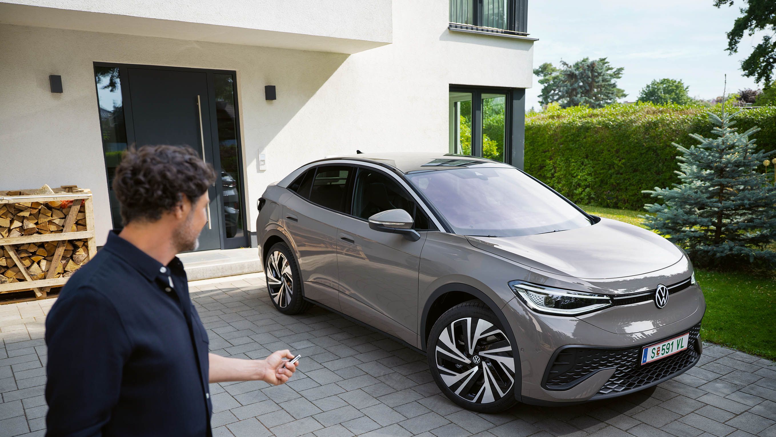 Ein grauer ID.5 steht in einer Einfahrt vor einem Haus, ein Mann schließt das Auto ab. 