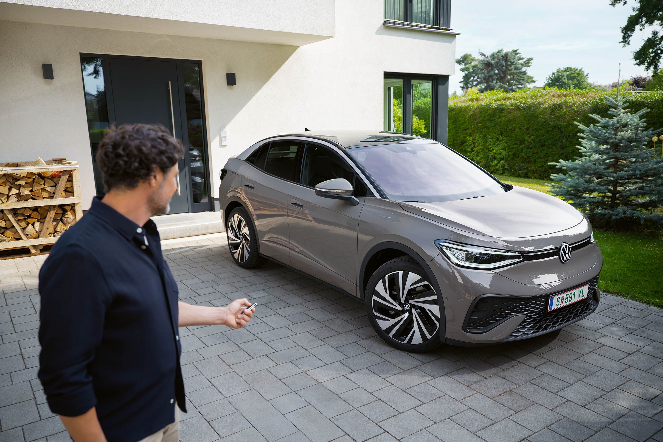 Ein grauer ID.5 steht in einer Einfahrt vor einem Haus, ein Mann schließt das Auto ab. 