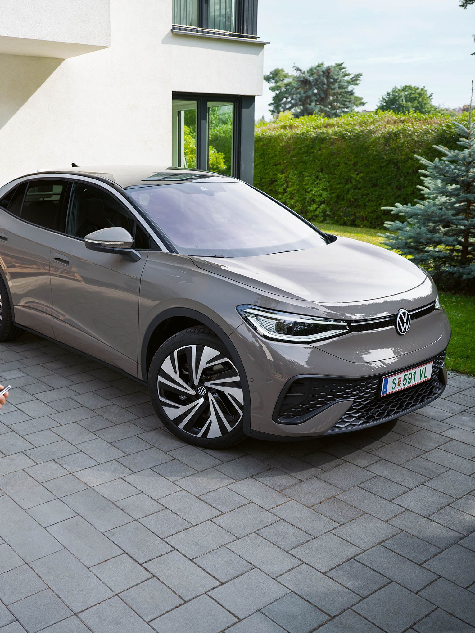 Ein grauer ID.5 steht in einer Einfahrt vor einem Haus, ein Mann schließt das Auto ab. 