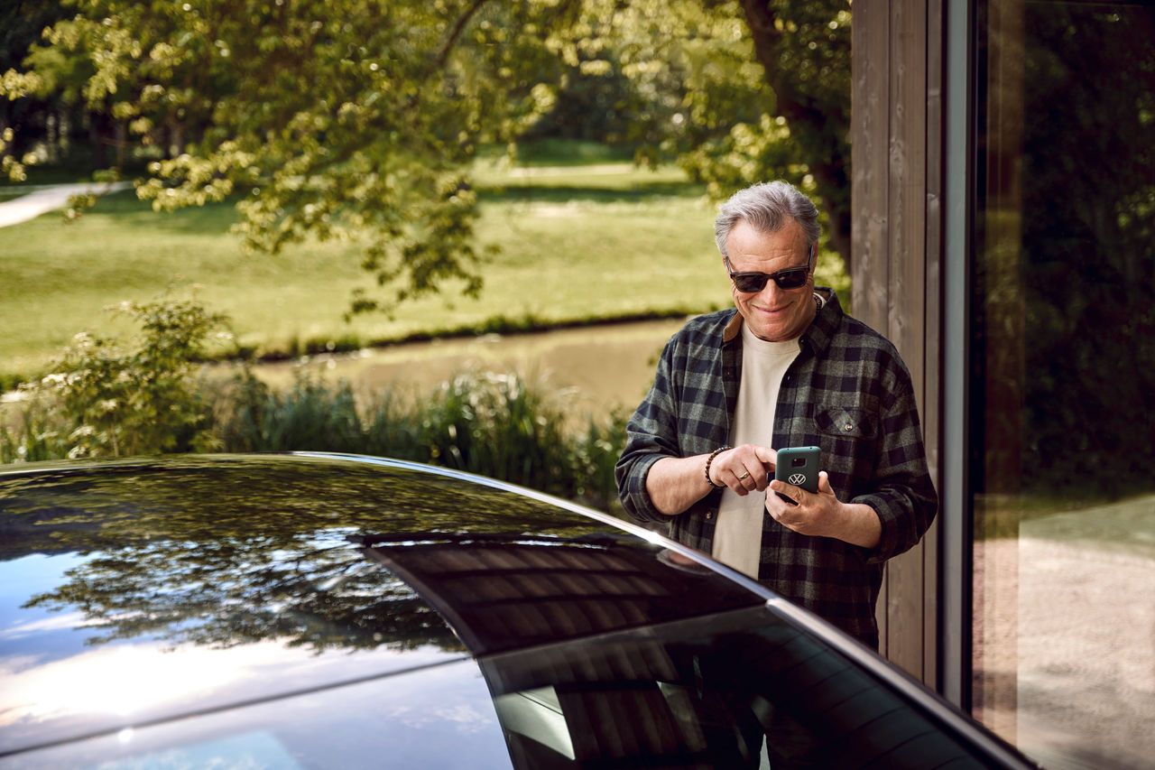 Moški stoji za Volkswagnom in gleda v svoj mobilni telefon.