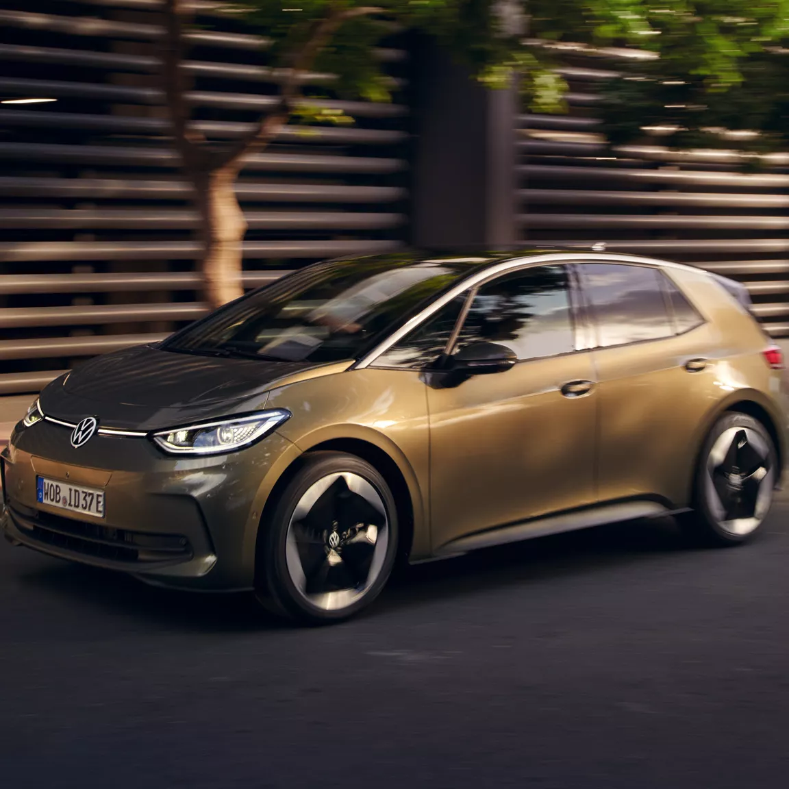 Slika prikazuje VW ID.3 v temni olivinsko zeleni kovinski barvi s platišči Sanya. Avtomobil je bočno parkiran ob robniku. 