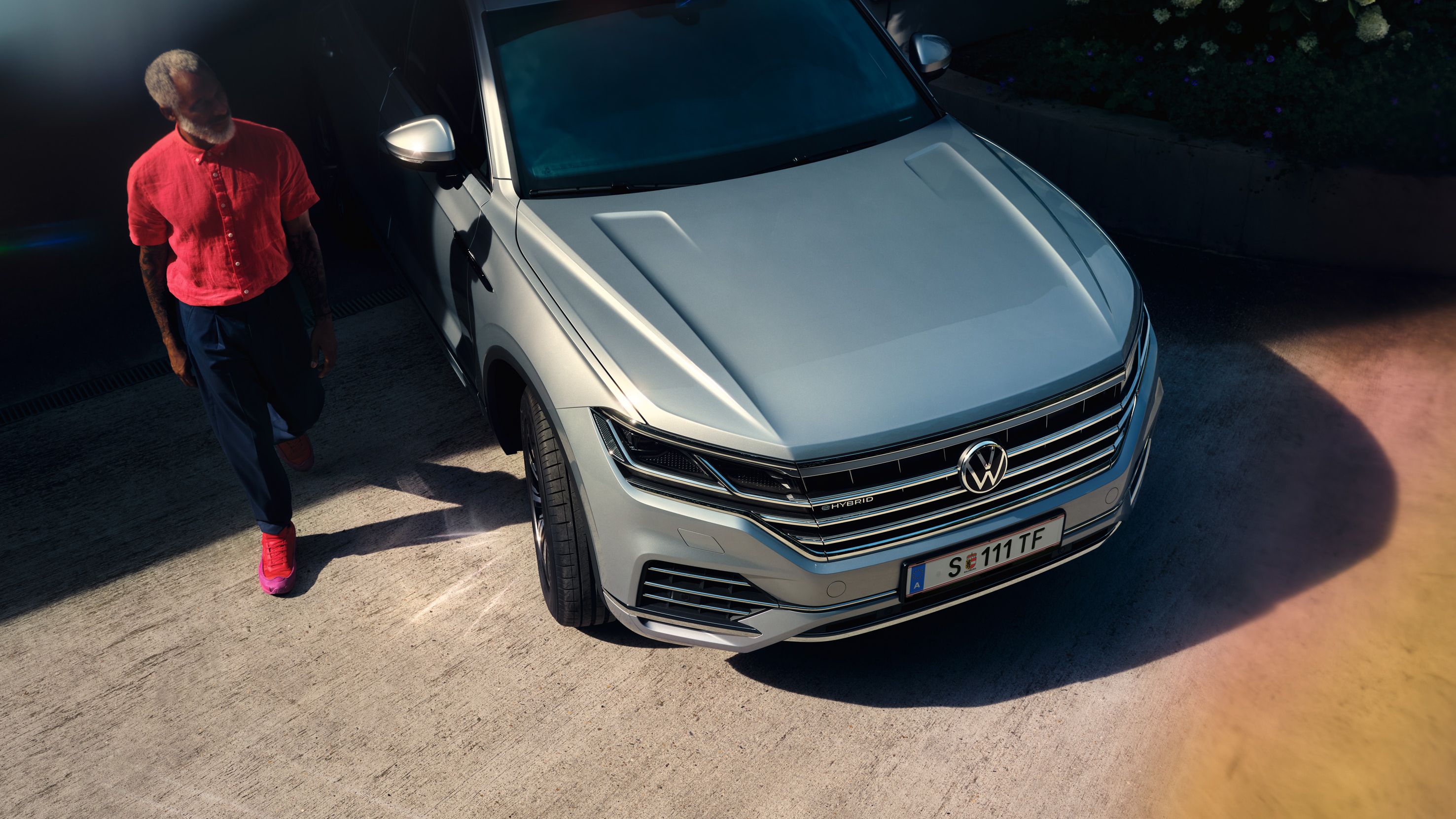 Volkswagen Touareg eHybrid srebrne barve, pogled od spredaj, stoji na dovozu, moški gre mimo