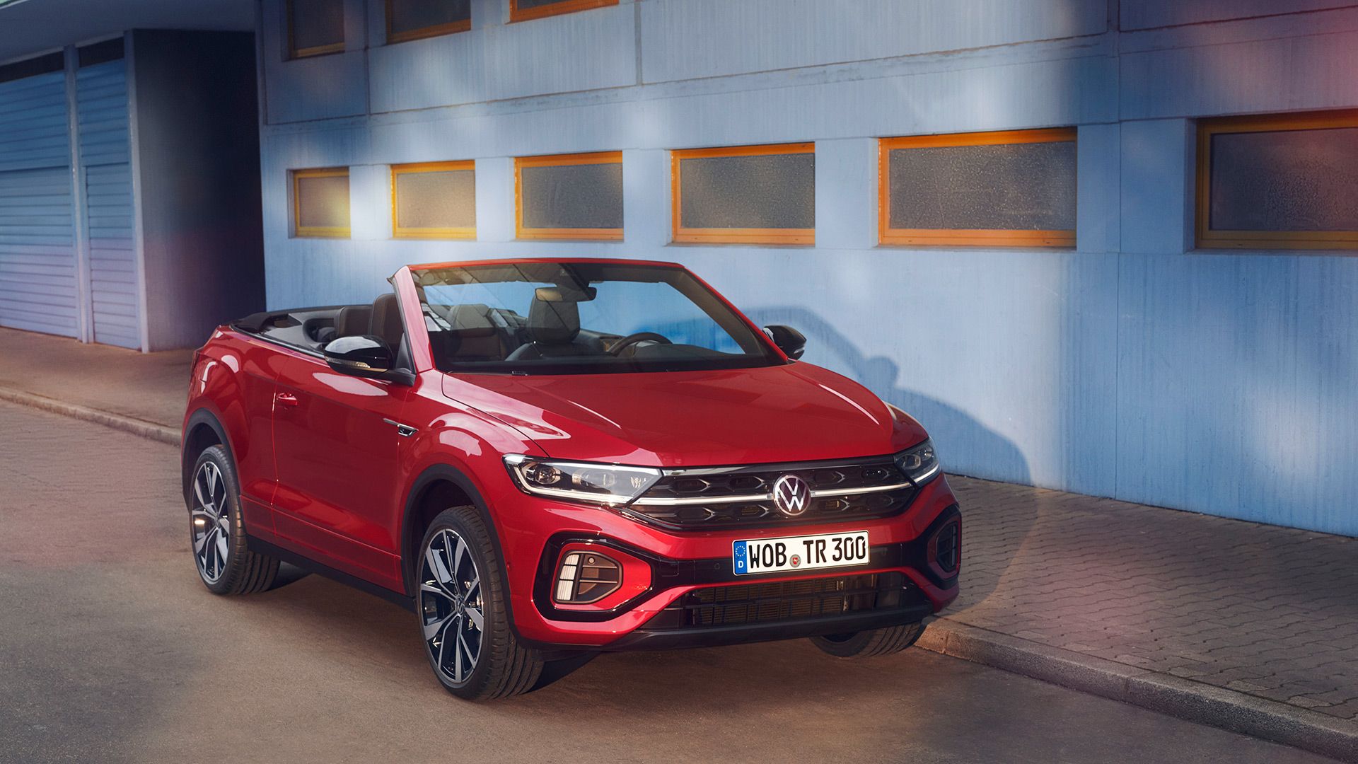 Sprednji in stranski del rdečega T-Roc Cabrioleta z odprto streho, parkiranega ob robu cestišča.