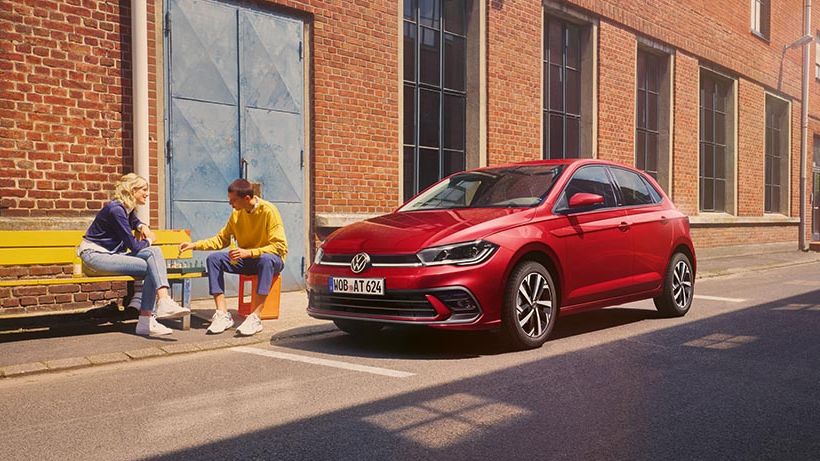 VW Polo Style v rdeči barvi parkiran pred industrijsko stavbo