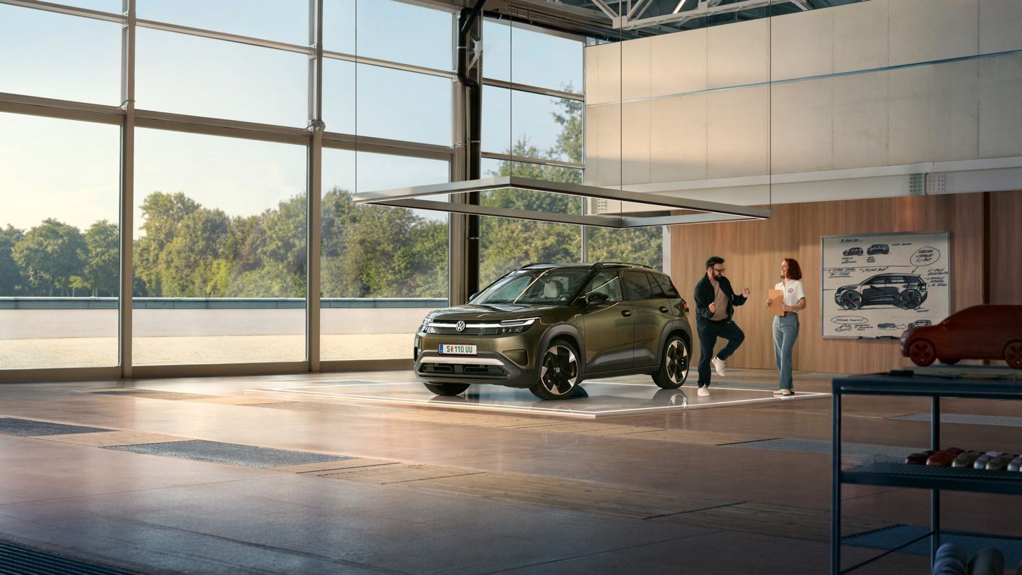 VW ID. Cross stoji v minimalistično opremljenem oblikovalskem studiu, ob njem pa poskakuje vznemirjen moški in se pogovarja z inženirko.