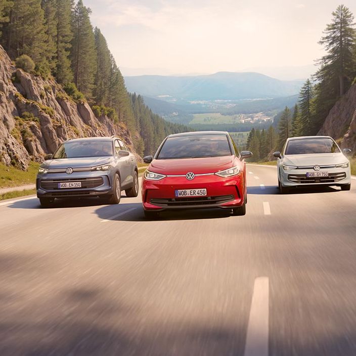 Volkswagen Tiguan, ID.3 in Golf se peljejo po cesti med hribi in gozdovi, vozijo se vzporedno. V ozadju je čudovita pokrajina z drevesi in daljno dolino.