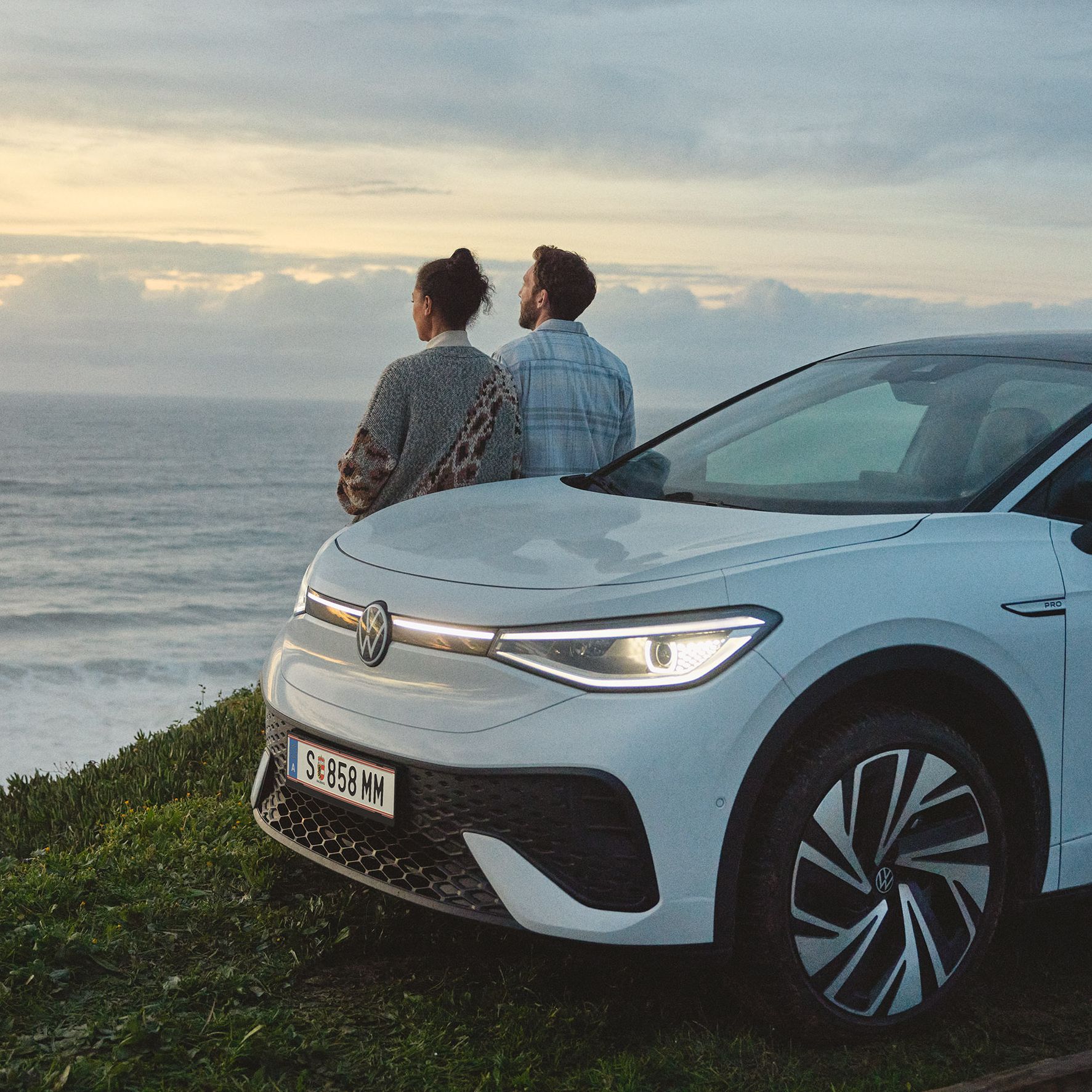 Ein ID.5 steht auf einer Wiese, der Blick geht aufs Meer. Ein Paar steht am Auto und blickt auf das Meer.