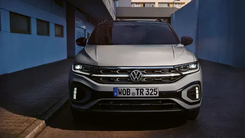 Sprednji del belega VW T-Roca R-Line, svetijo dnevne LED-luči in opcijska, osvetljena mreža hladilnika.