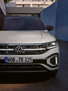 Sprednji del belega VW T-Roca R-Line, svetijo dnevne LED-luči in opcijska, osvetljena mreža hladilnika.