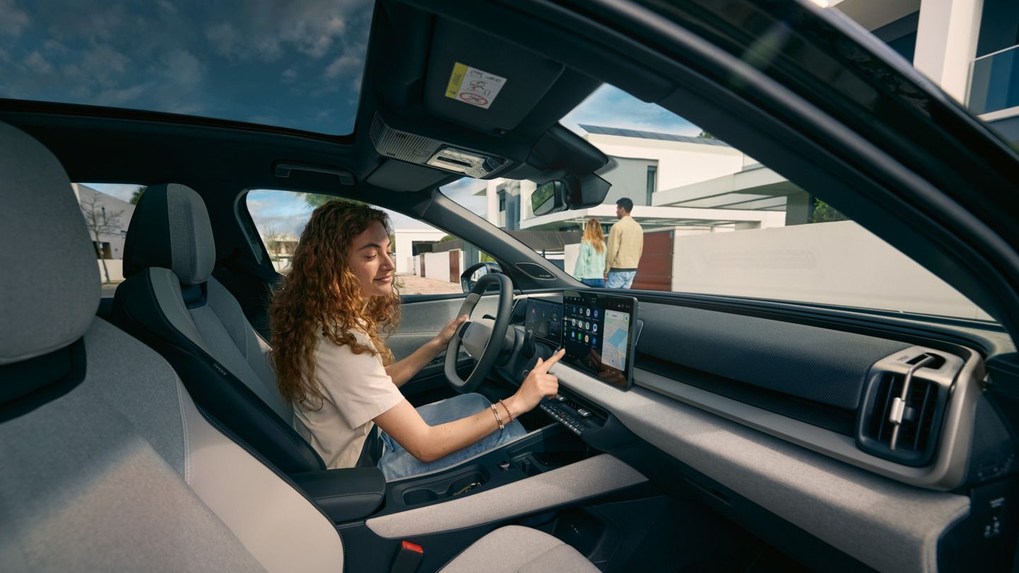 Mlada ženska sedi na voznikovem sedežu VW ID. Cross in upravlja informacijsko-zabavni sistem.