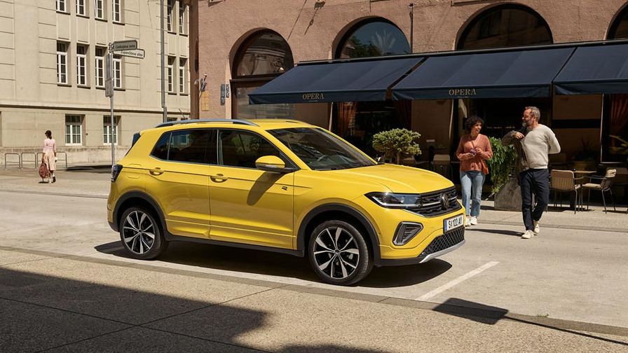 Rumen VW T-Cross je parkiran pred mestno ulično kavarno. Približuje se mu par. Avto je prikazan od strani.