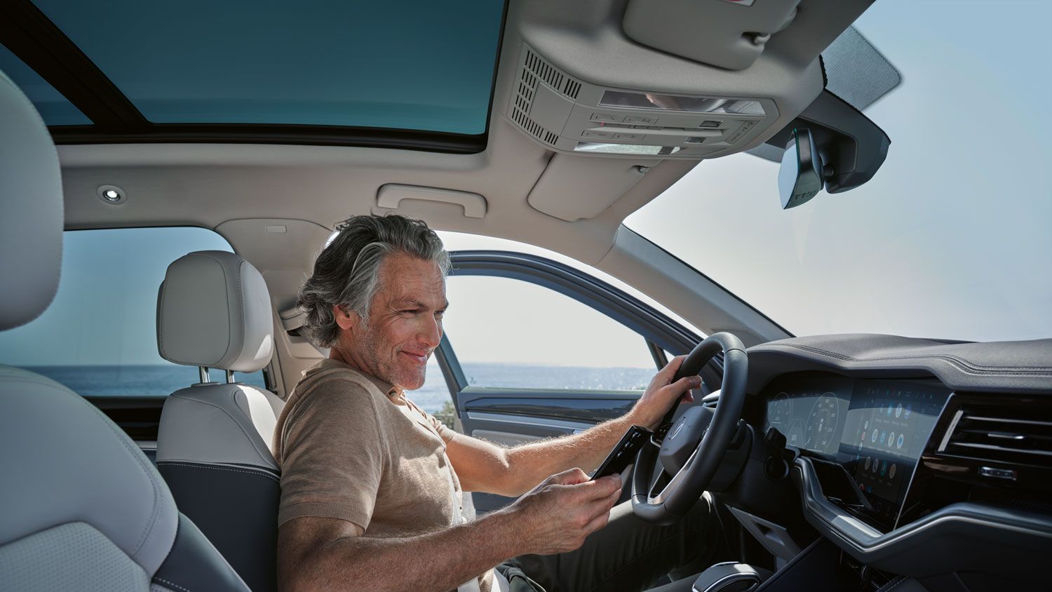 Moški v parkiranem vozilu VW Touareg Elegance poveže svoj pametni telefon z vozilom VW Touareg Elegance prek sistema Wireless App Connect.