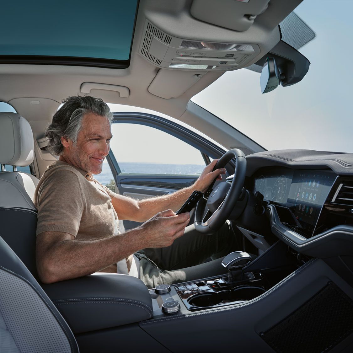Moški v parkiranem vozilu VW Touareg Elegance poveže svoj pametni telefon z vozilom VW Touareg Elegance prek sistema Wireless App Connect.