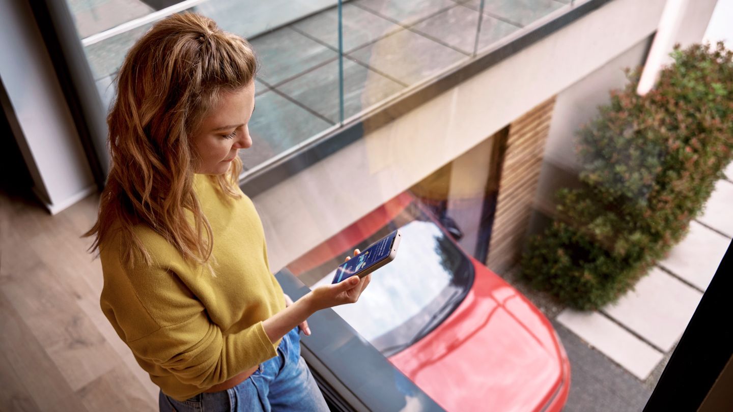 Frau schaut zu Hause auf ihr Smartphone, während ihr Tiguan in der Einfahrt geparkt ist.