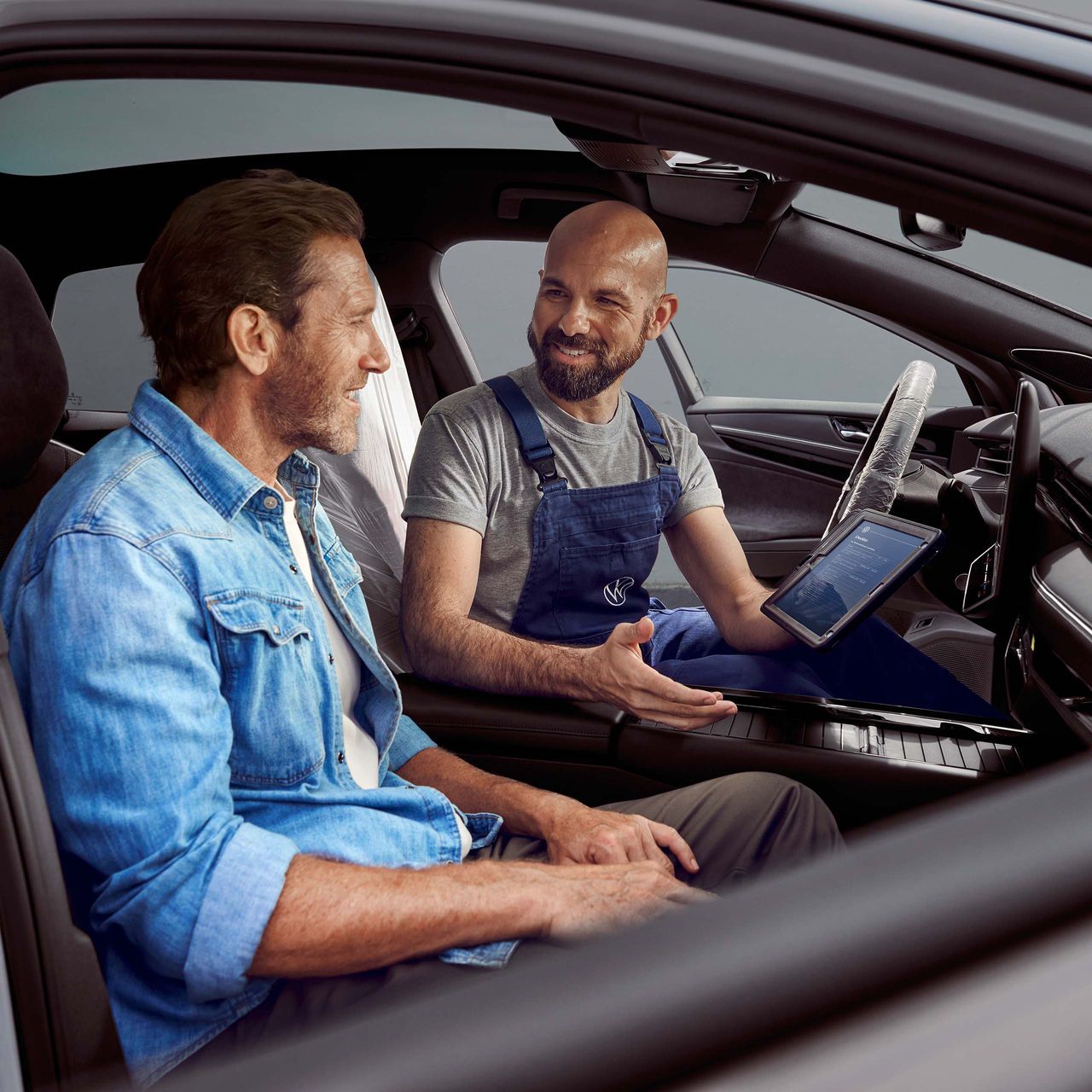 Stranka sedi v vozilu, uslužbenec servisa VW nekaj razlaga na tablici