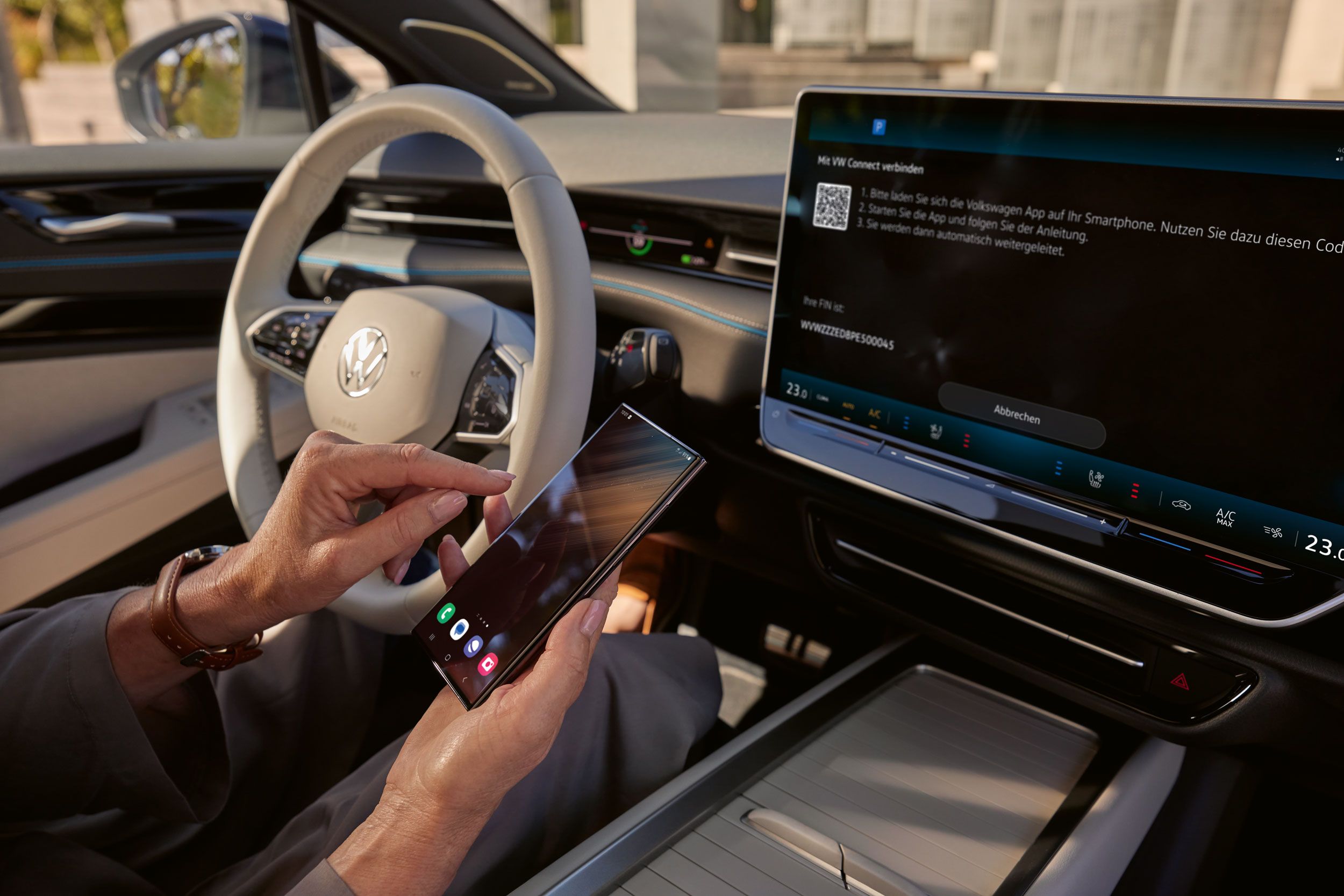 Pogled na armaturno ploščo v ID.7. Nekdo prek VW Connect povezuje pametni telefon z vozilom. Na zaslonu infotainment sistema je vidna povezava s VW Connect. 