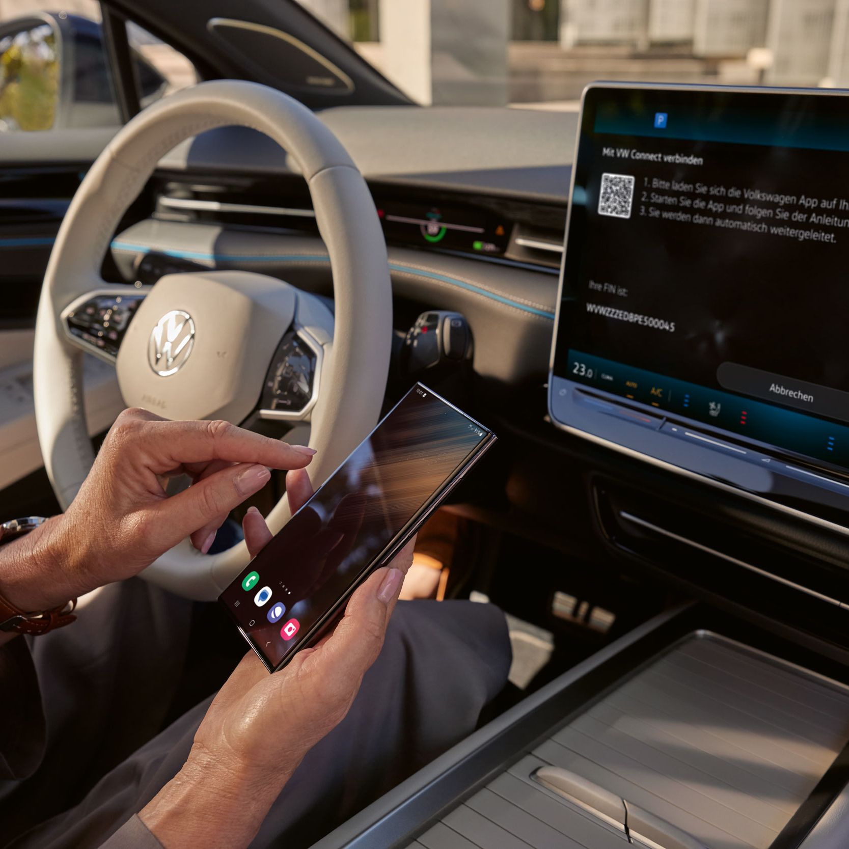 Pogled na armaturno ploščo v ID.7. Nekdo prek VW Connect povezuje pametni telefon z vozilom. Na zaslonu infotainment sistema je vidna povezava s VW Connect. 