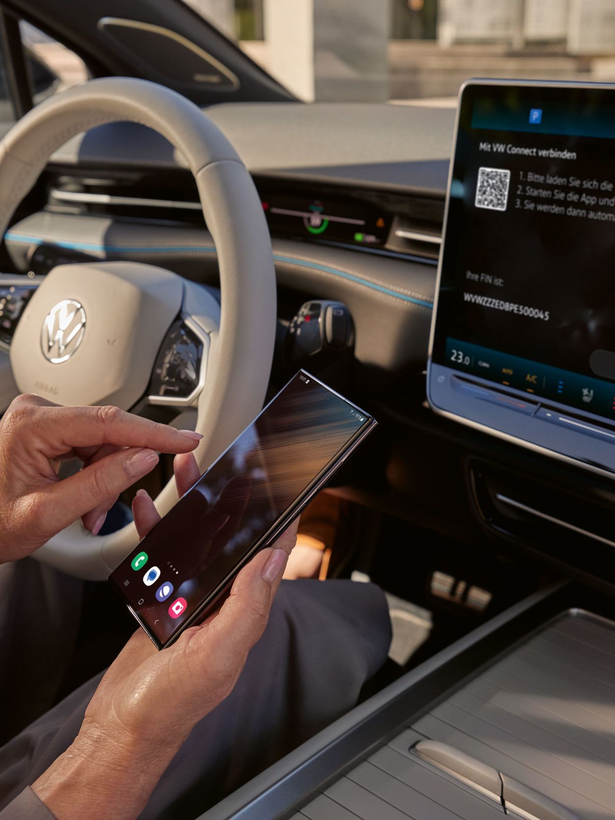 Pogled na armaturno ploščo v ID.7. Nekdo prek VW Connect povezuje pametni telefon z vozilom. Na zaslonu infotainment sistema je vidna povezava s VW Connect. 