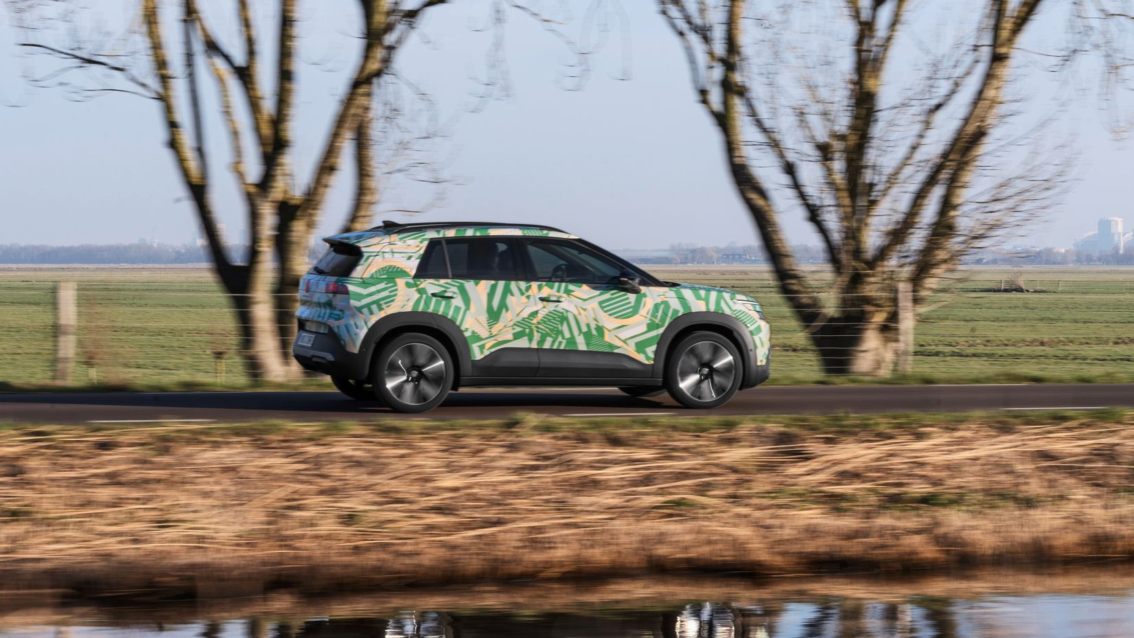 VW ID. Cross z maskirno folijo je od strani prikazan med vožnjo po regionalni cesti.
