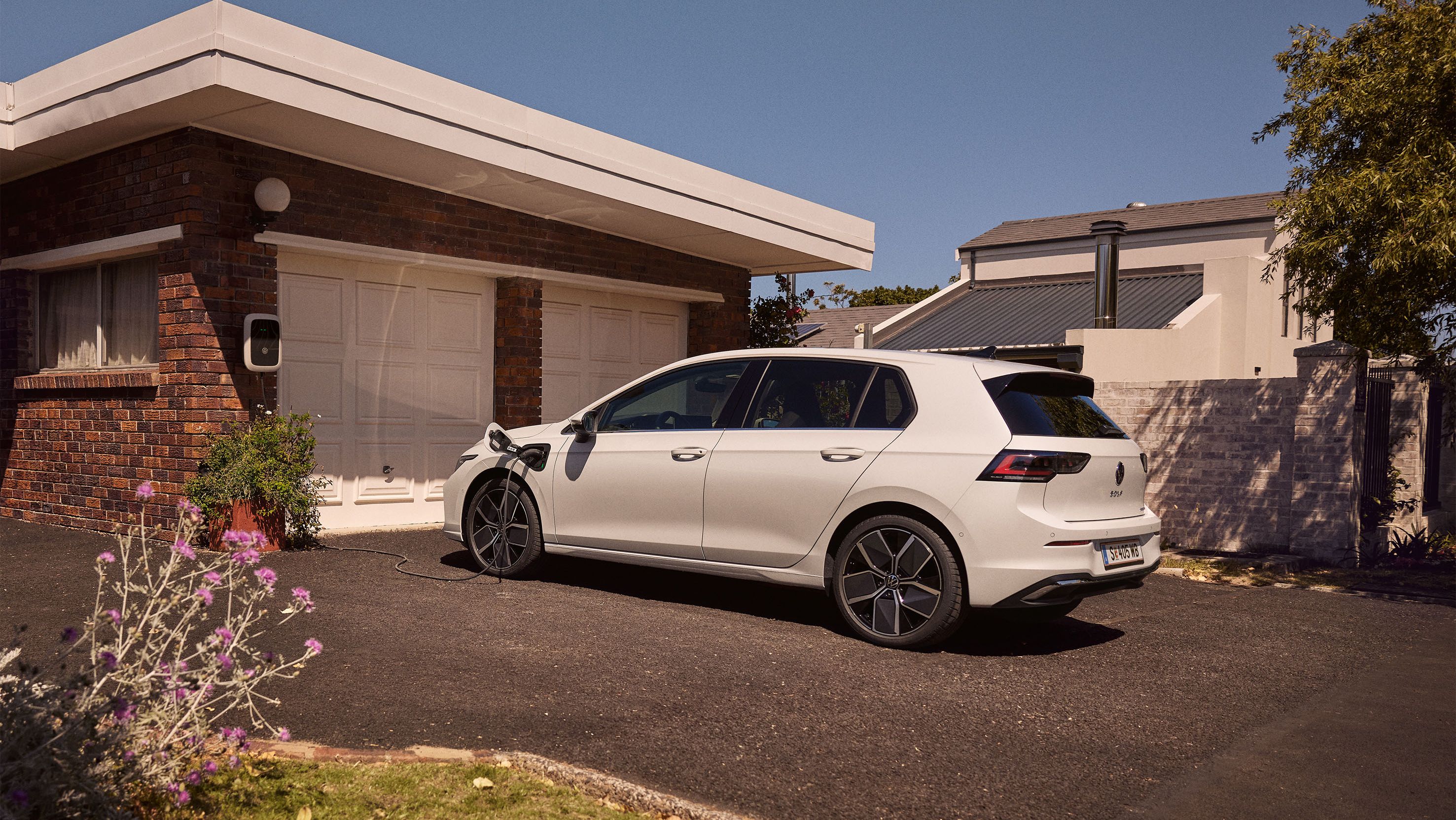 Ein weißer VW Golf 8 eHybrid steht geparkt vor einer Garage und wird aufgeladen. 