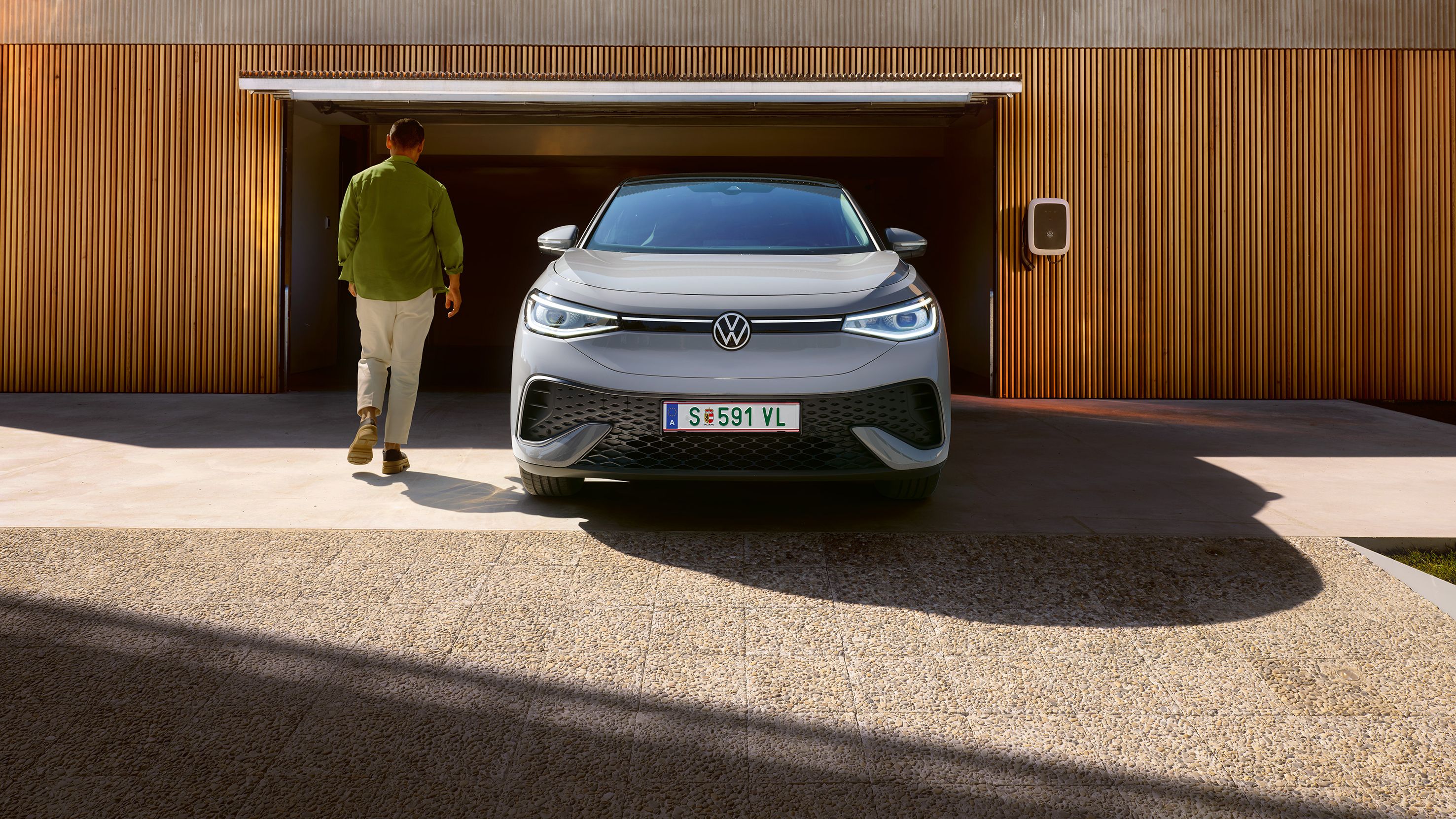 Siv VW ID.5 od spredaj pred garažo, moški gre mimo avta