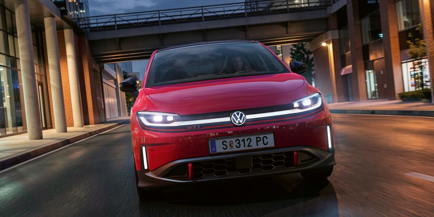 Oseba zvečer vozi rdeč VW ID. Polo GTI skozi sodobno osvetljeno poslovno četrt.
