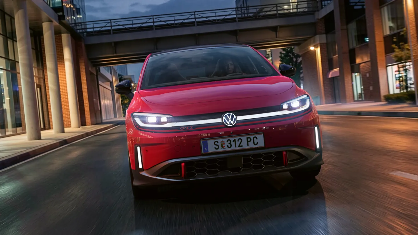 Oseba zvečer vozi rdeč VW ID. Polo GTI skozi sodobno osvetljeno poslovno četrt.