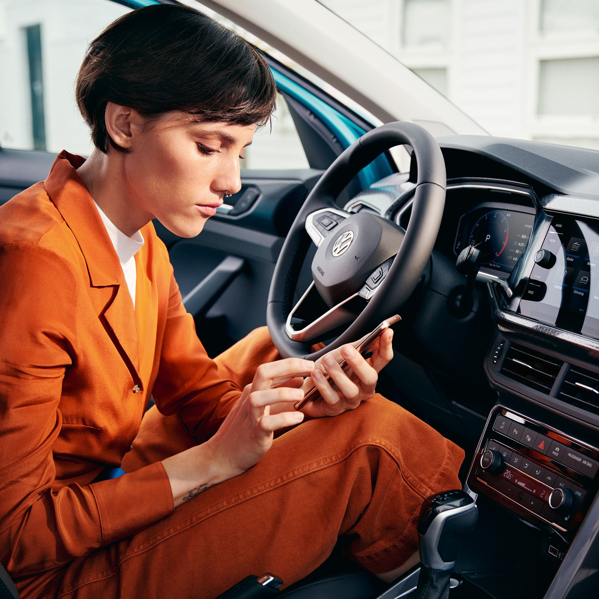 Ženska v vozilu VW T-Cross z mobilnim telefonom v roki in odprtimi vrati.