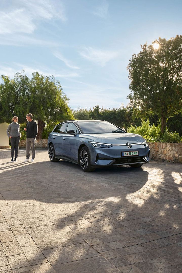 Der VW ID.7 Tourer ist vor Einfamillienhaus geparkt, eine Frau und ein Mann stehen neben ihm und unterhalten sich