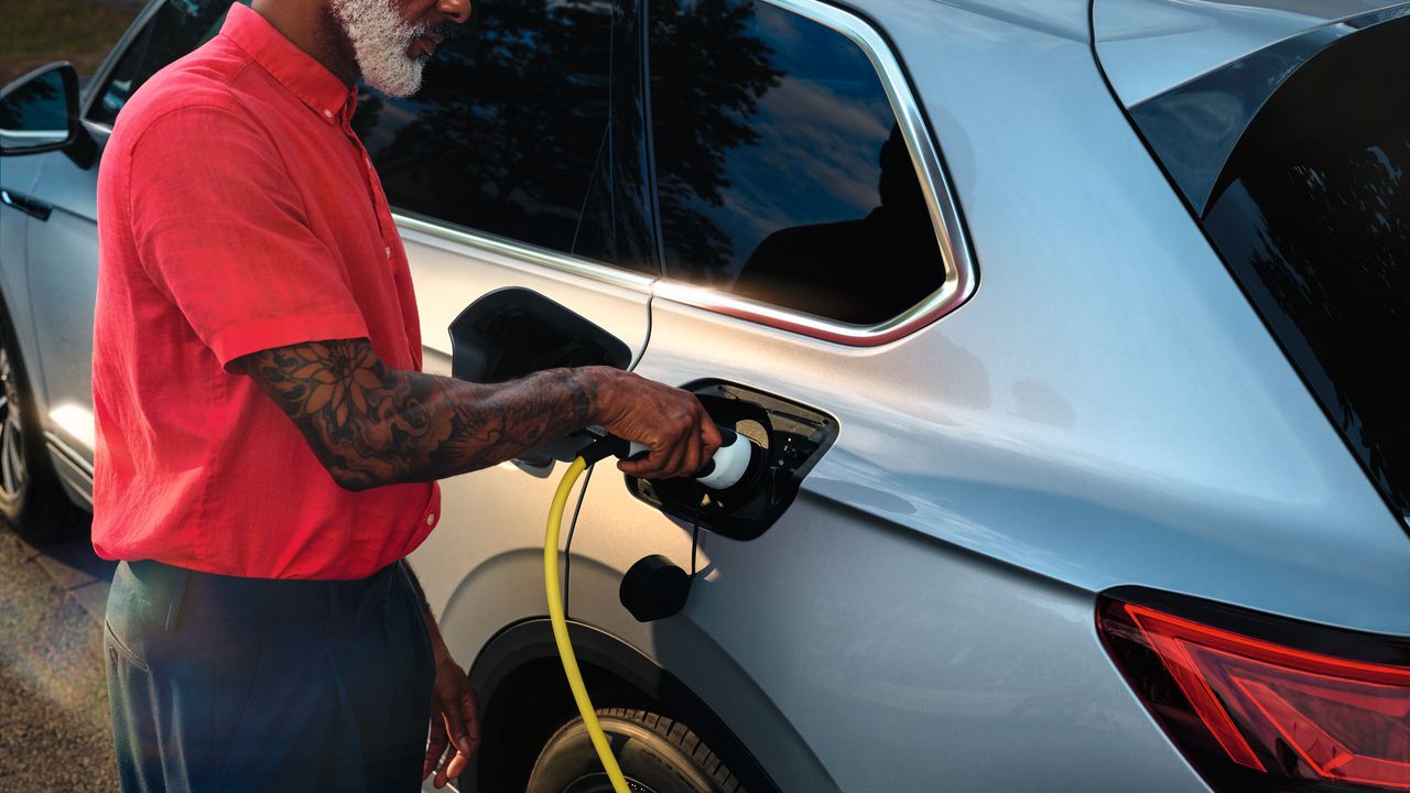 Volkswagen Touareg eHybrid srebrne barve, pogled na stranski del/zadek, moški priklaplja polnilni kabel