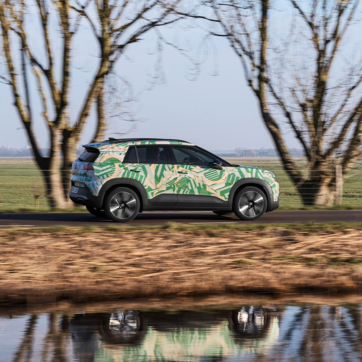 VW ID. Cross z maskirno folijo je od strani prikazan med vožnjo po regionalni cesti.