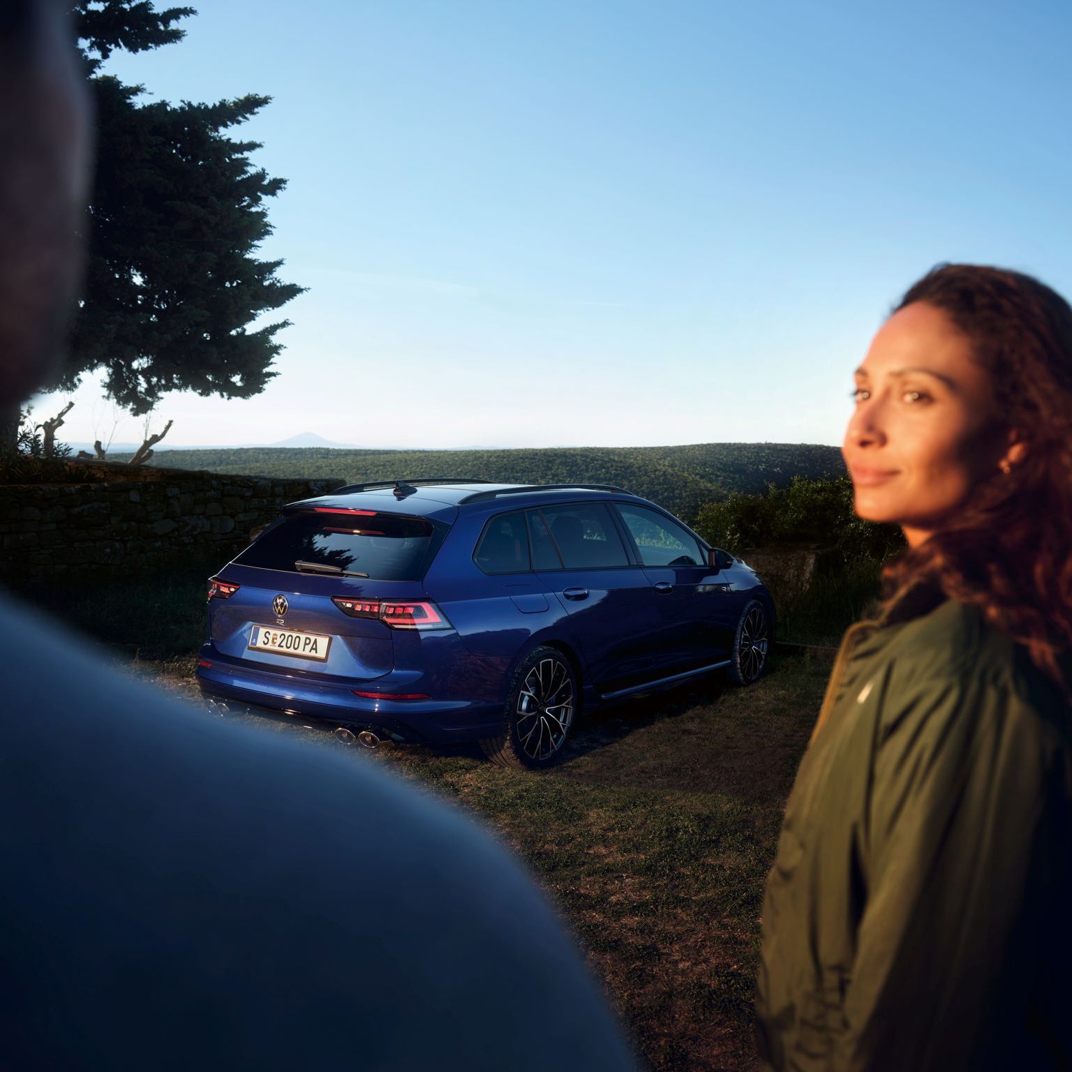 Ein roter VW Golf GTI steht vor einem Gebäude. Zwei Personen sitzen neben dem Wagen.