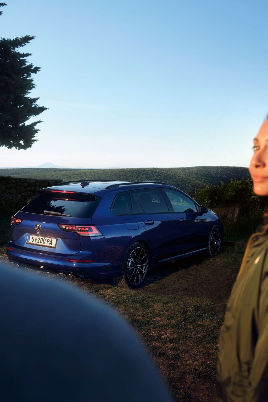 Ein roter VW Golf GTI steht vor einem Gebäude. Zwei Personen sitzen neben dem Wagen.