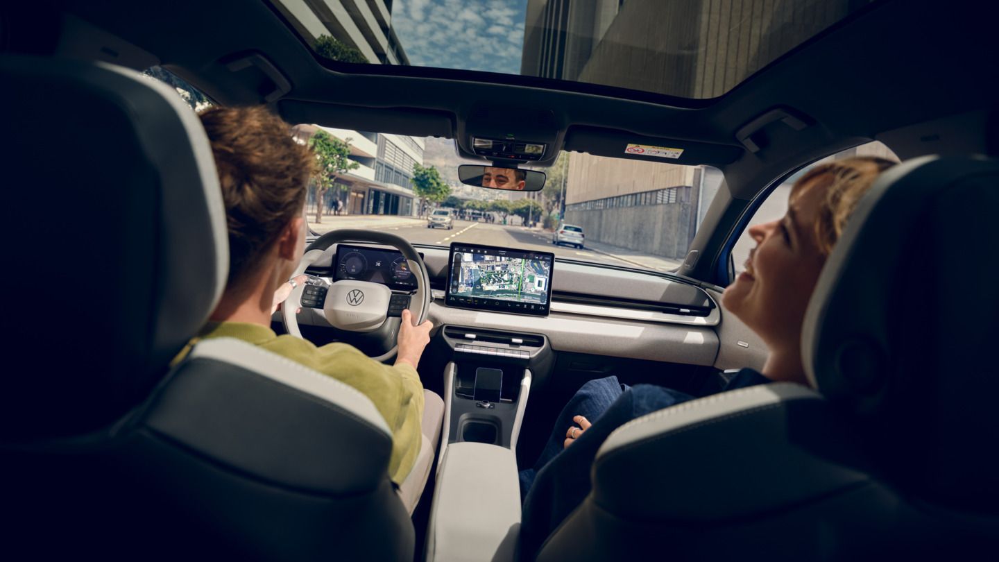 Moški vozi VW ID. Polo Style, na sovoznikovem sedežu ženska, ki se smeji. Visoke stavbe so vidne skozi panoramsko streho