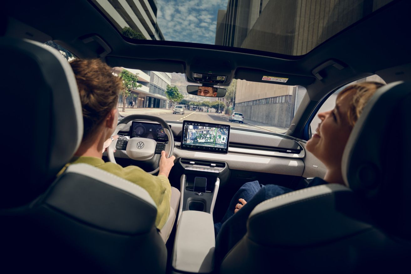 Moški vozi VW ID. Polo Style, na sovoznikovem sedežu ženska, ki se smeji. Visoke stavbe so vidne skozi panoramsko streho