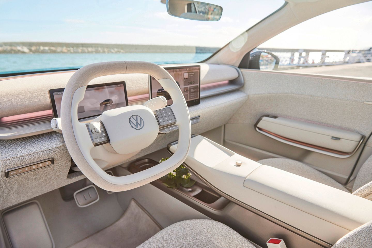 Slika prikazuje notranjost ID. Cross z svetlo sivim oblazinjenjem. Volan je nameščen na sredini, na armaturni plošči pa je več digitalnih zaslonov. V ozadju je skozi vetrobransko steklo viden pogled na vodo.