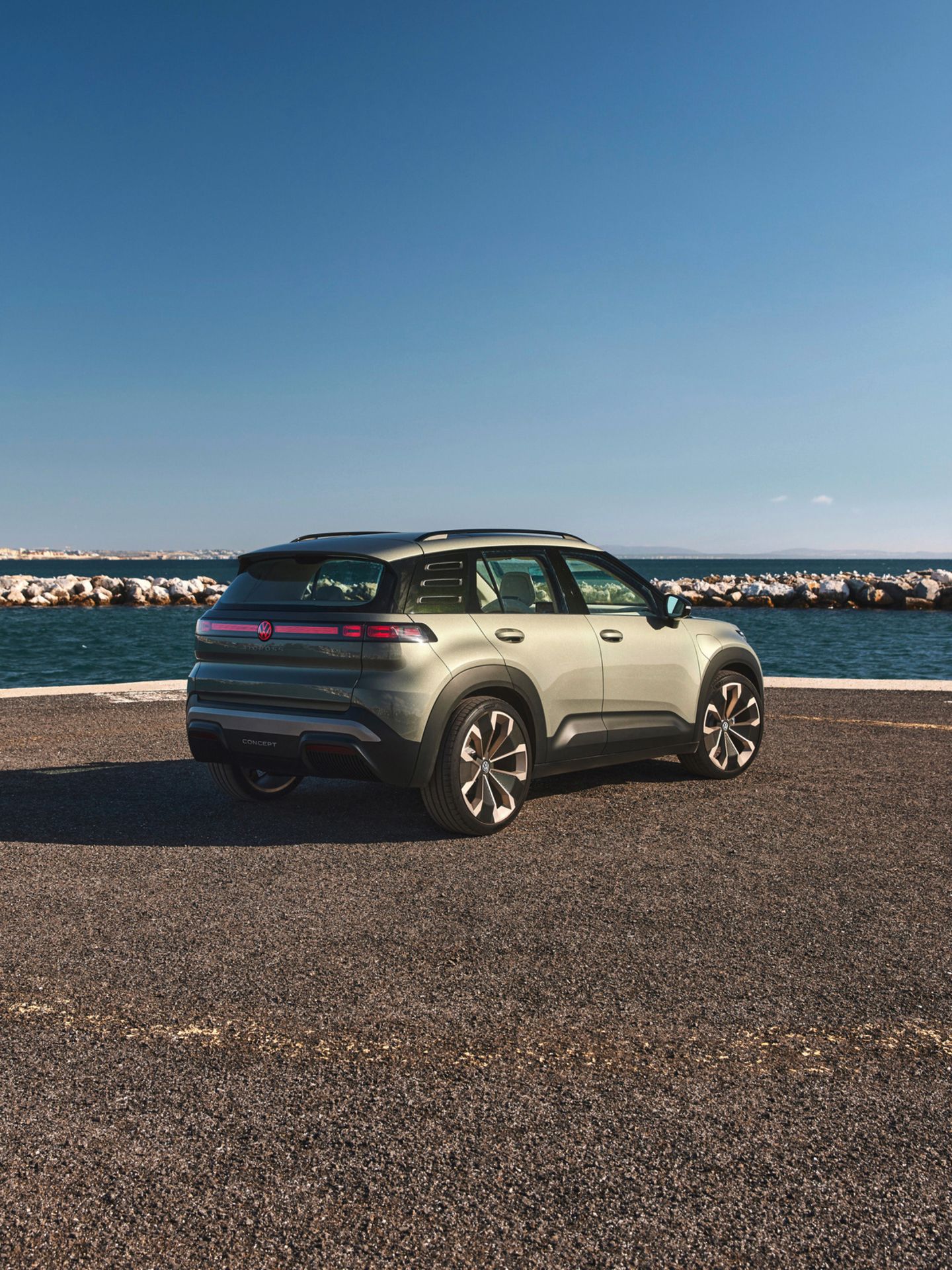 Zeleni VW ID. Cross stoji ob obalni cesti z razgledom na morje in modro nebo brez oblakov. 