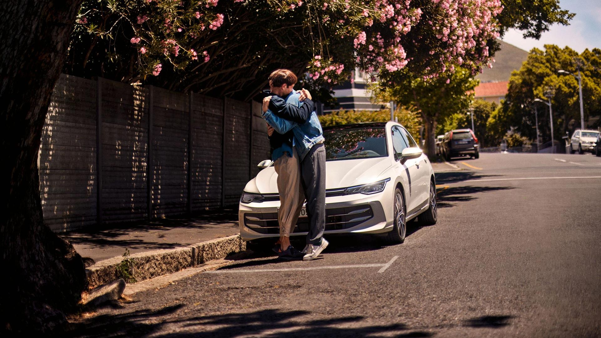 "Bel VW Golf. Dva moška objeta stojita poleg avtomobila "
