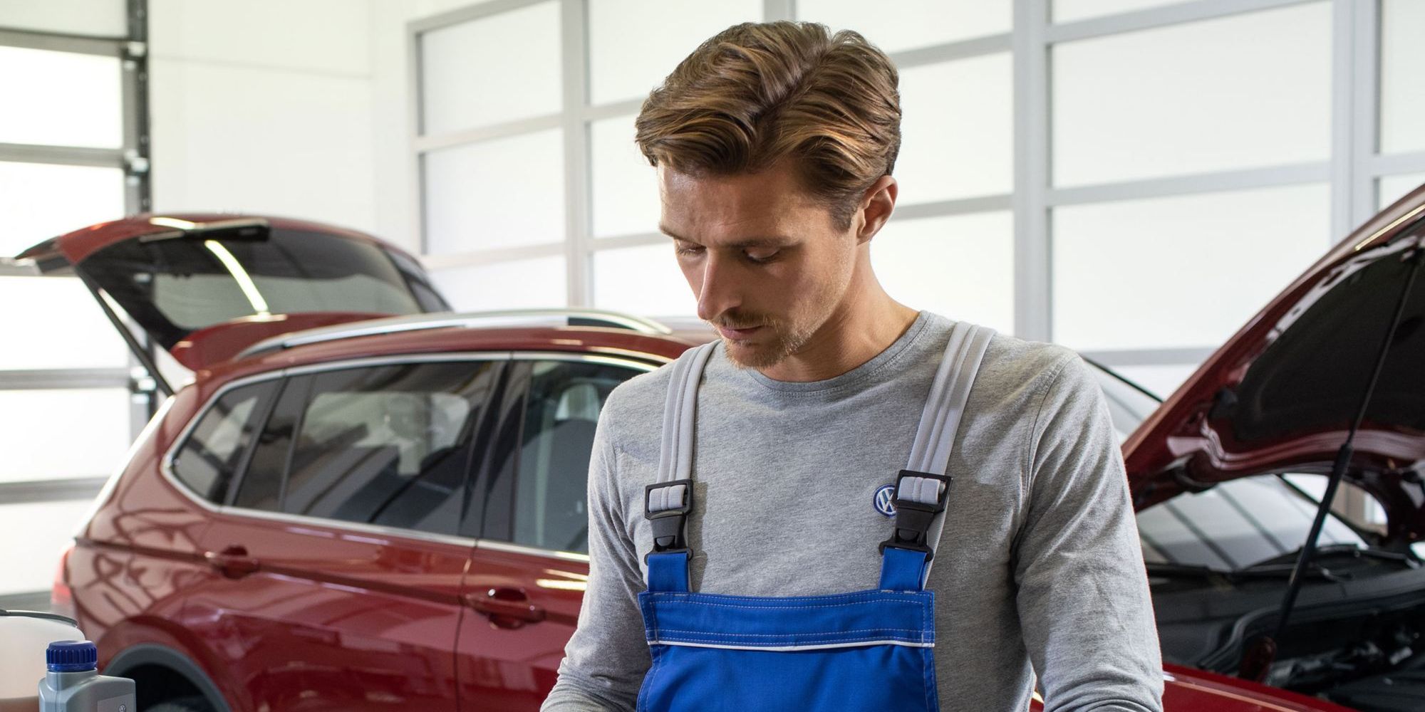 Ein VW Servicemitarbeiter vor einem roten Volkswagen mit Dieselmotor und einer geöffneten Motorhaube in einer Werkstatt