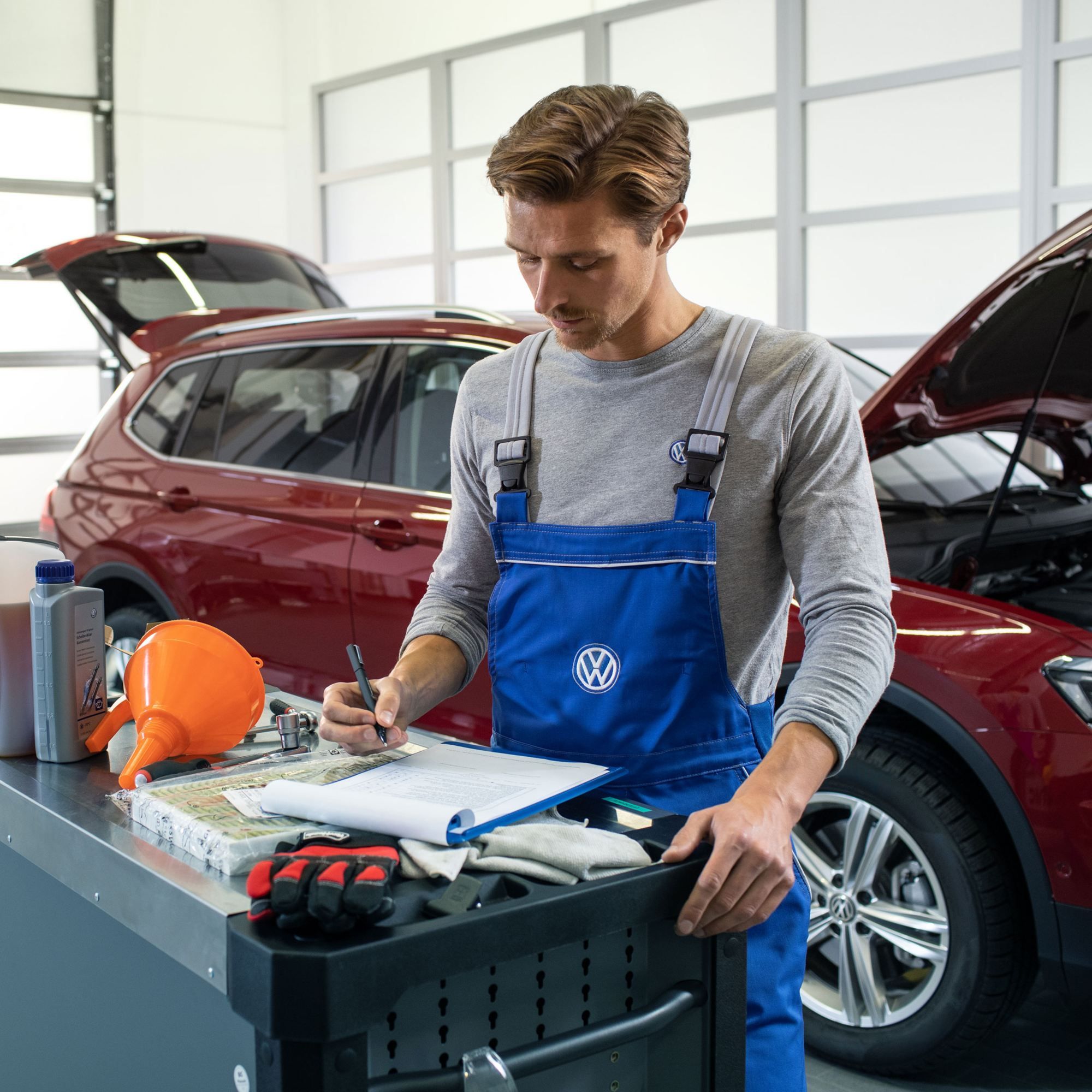 Servisni tehnik pred rdečim Volkswagnom Tiguan z dizelskim motorjem in odprtim pokrovom motorja v delavnici.