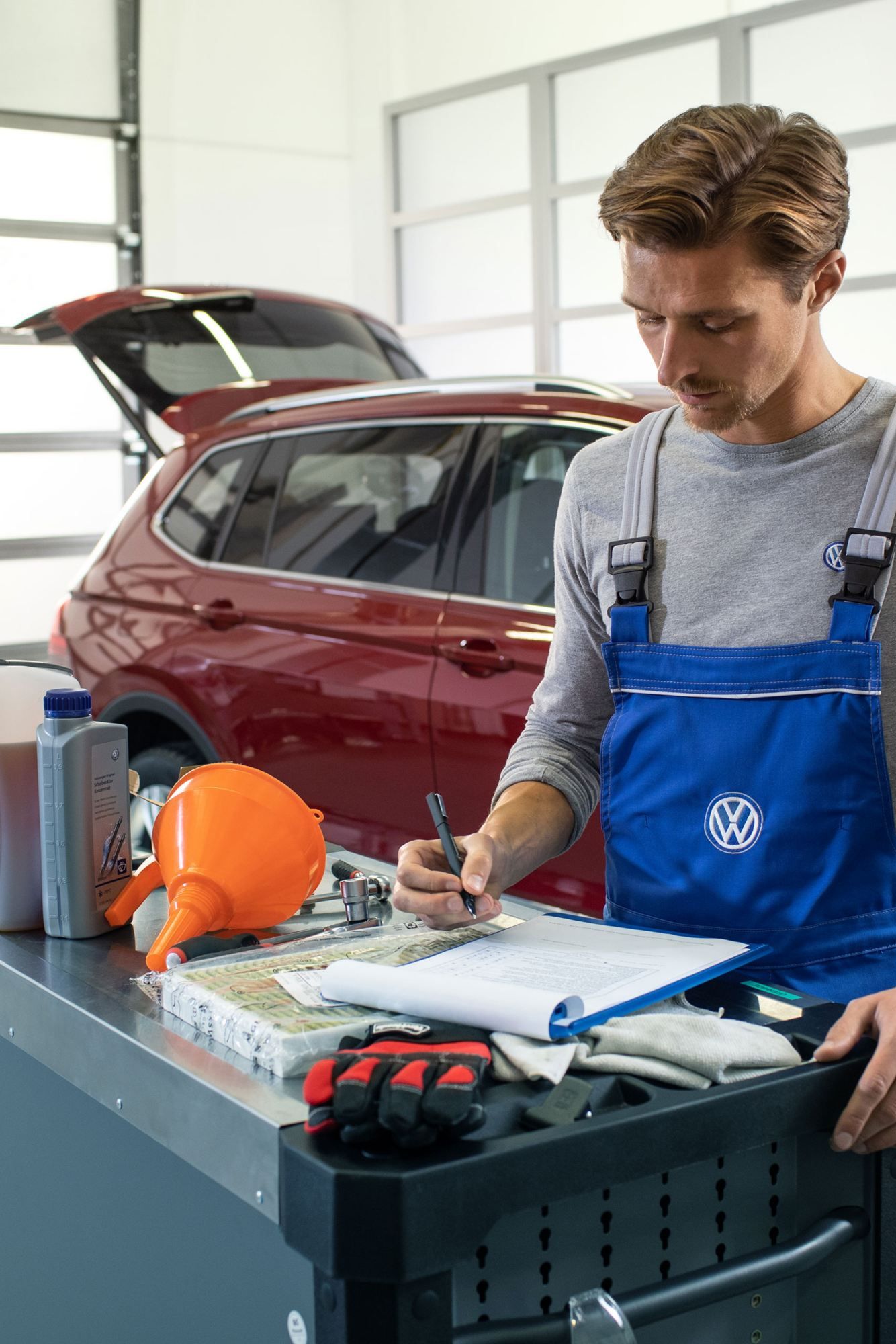 Ein VW Servicemitarbeiter vor einem roten Volkswagen mit Dieselmotor und einer geöffneten Motorhaube in einer Werkstatt