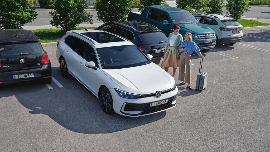 Dve ženski ob belem VW Passatu, ki samodejno parkira s pomočjo opcijskega sistema Park Assist Plus. Ena od žensk drži v roki pametni telefon.