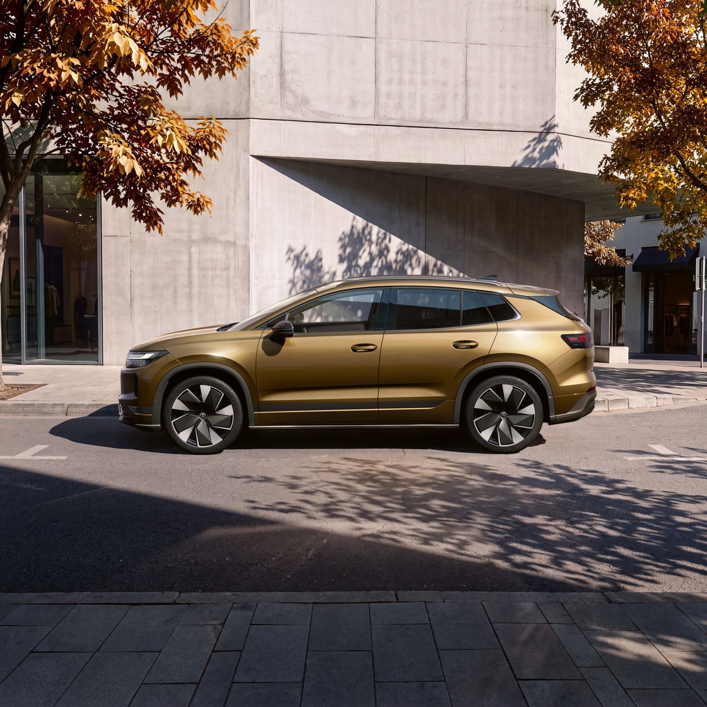 Stranski pogled na olivno-bronast VW ID. Tiguan, parkiran pred sodobno stavbo.
