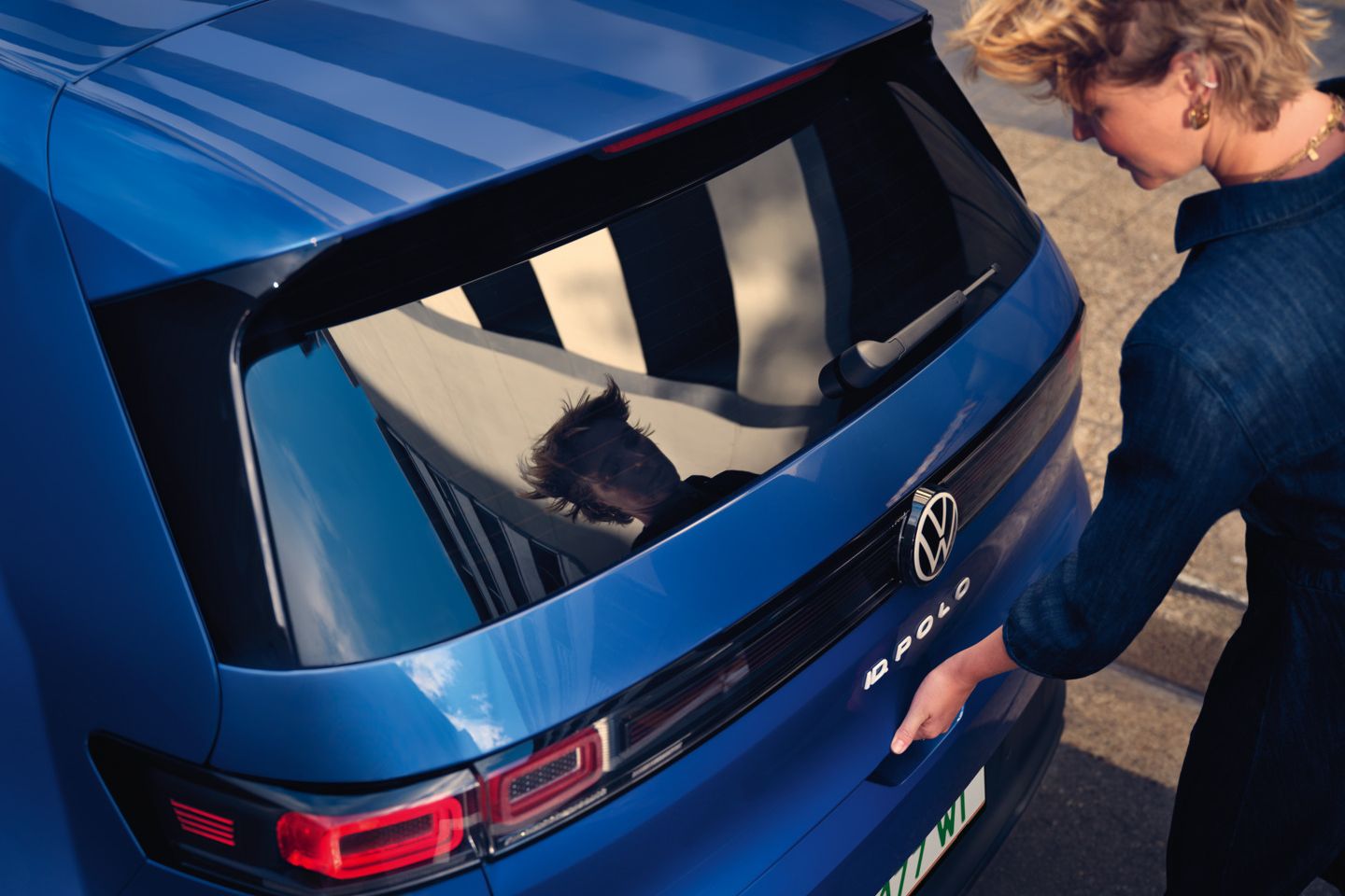 Ženska odpre pokrov prtljažnika modrega VW ID-ja. Polo Style.