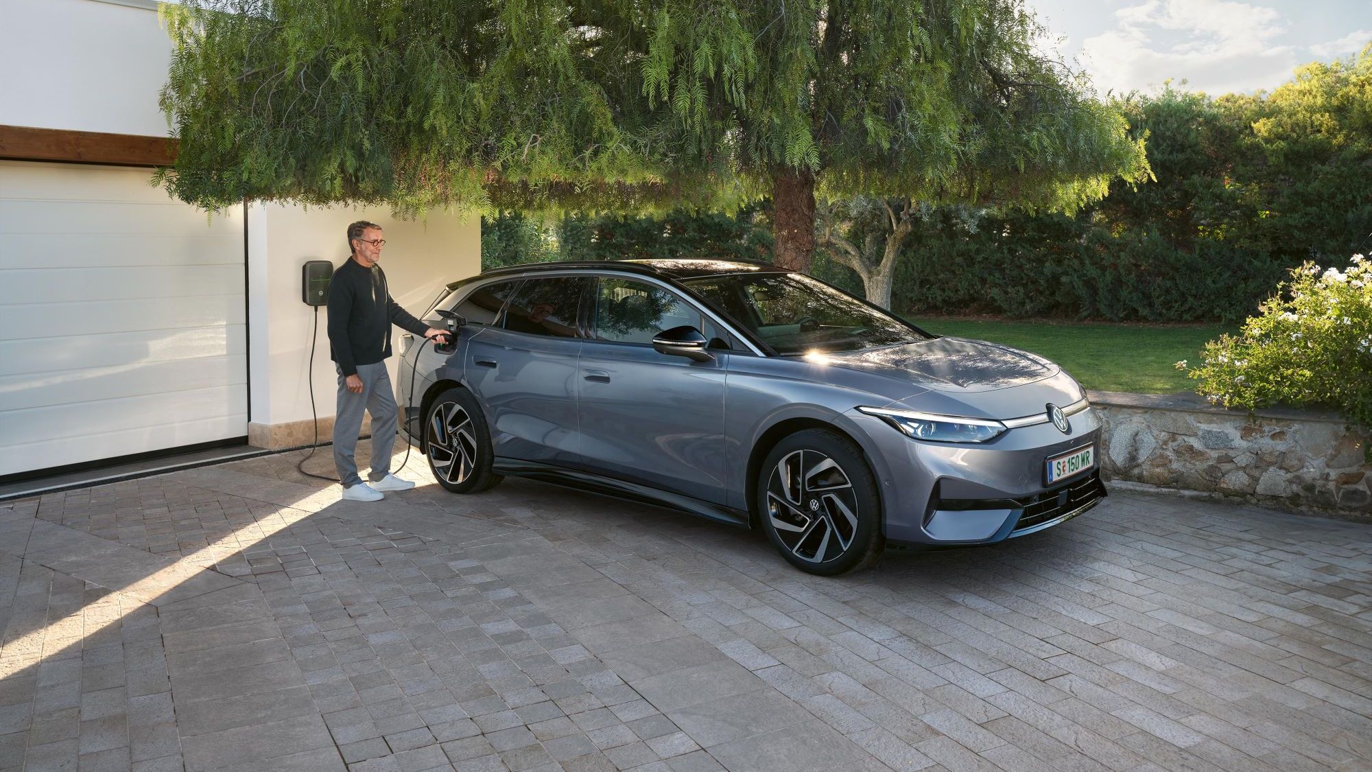  Moški stoji pred stensko polnilno postajo in polni svoj VW ID. 7 Tourer.