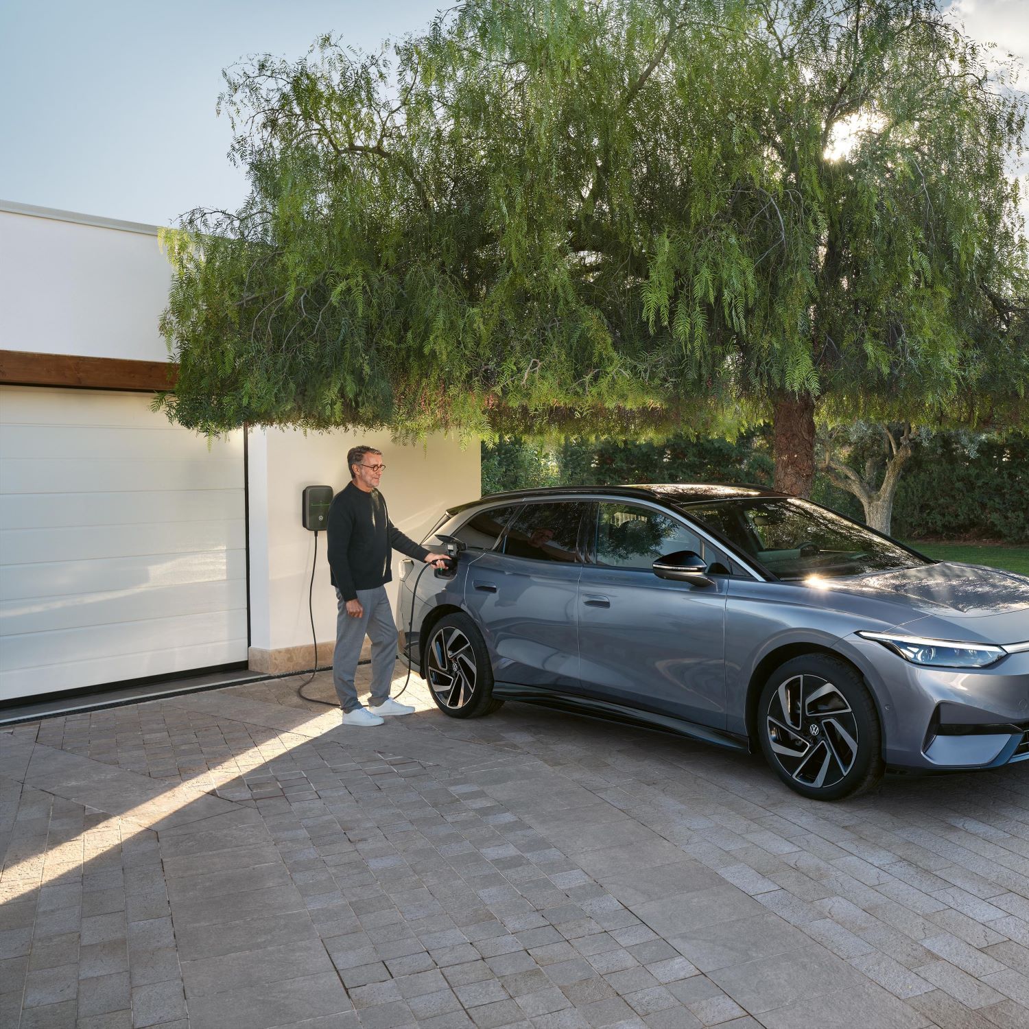  Moški stoji pred stensko polnilno postajo in polni svoj VW ID. 7 Tourer.