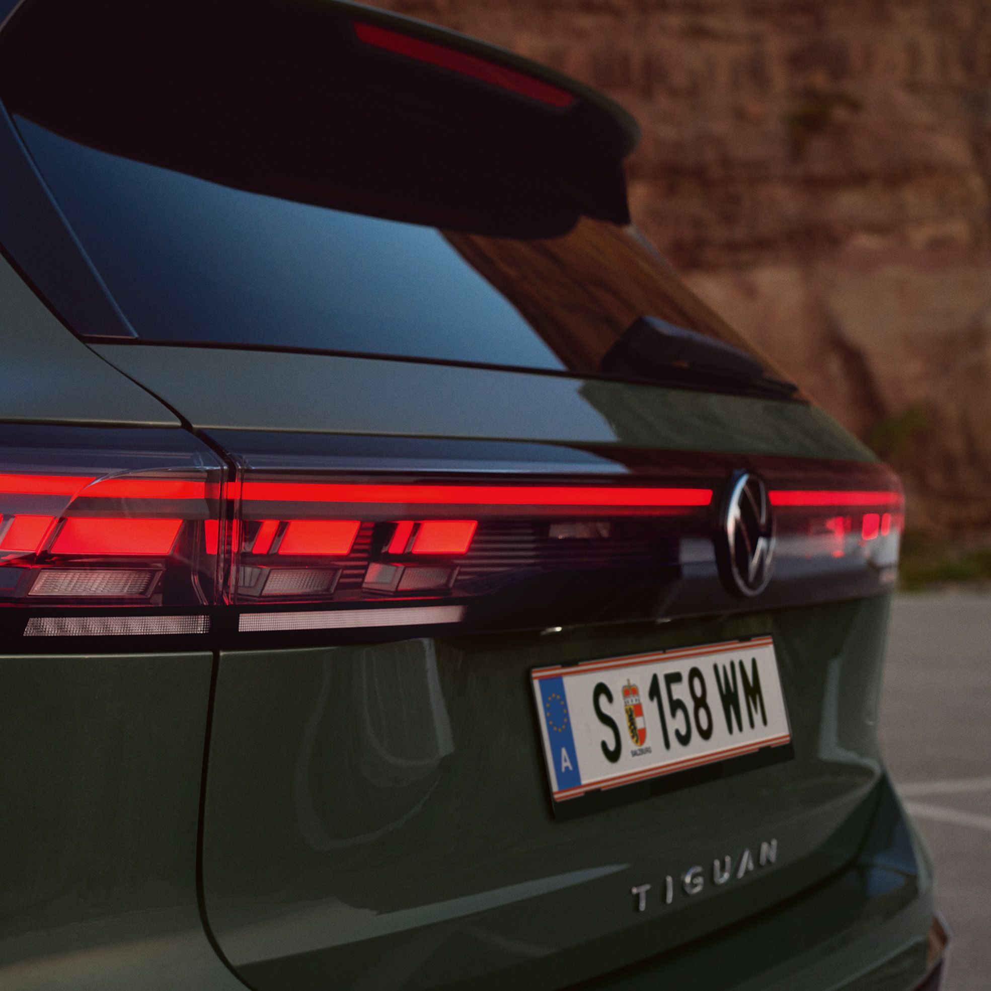 Detajlni posnetek svetlobne grafike zadnjih luči temnozelenega VW Tiguana, parkiranega pred skalnato pokrajino.